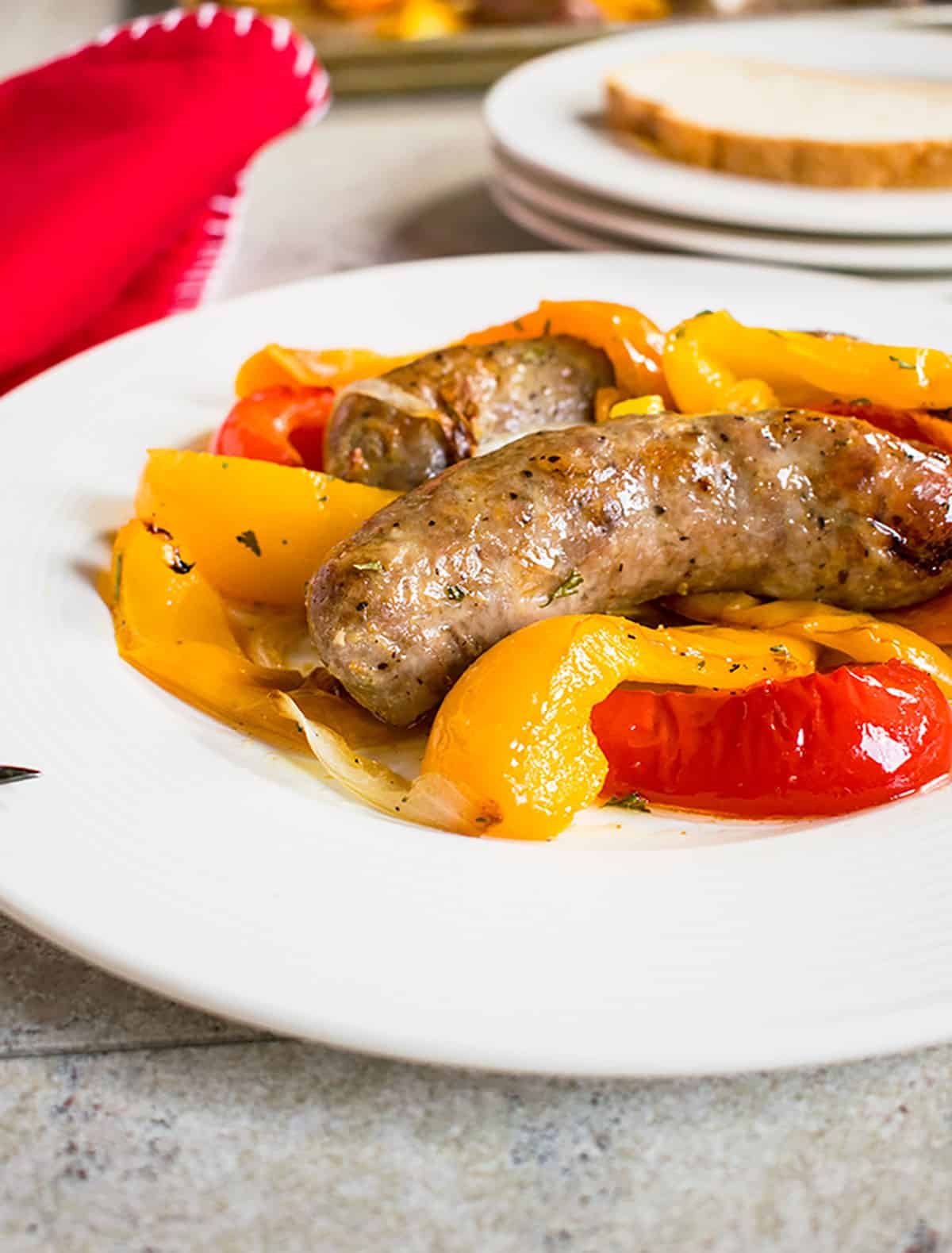 sausage, yellow and red peppers on white plate, red napkin, bread in background