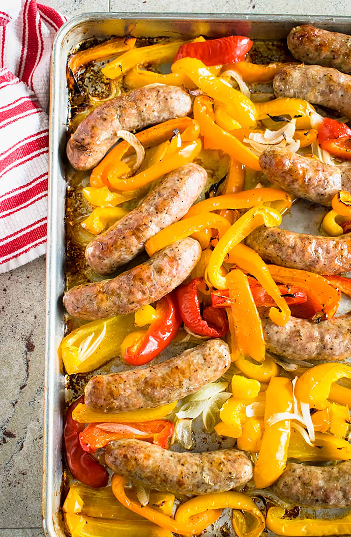overhead view of cooked sausages, peppers, onions on sheet pan, white and red striped cloth