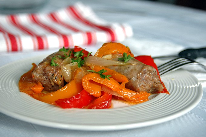 frontal view of cooked sausage, peppers, onions on white plate