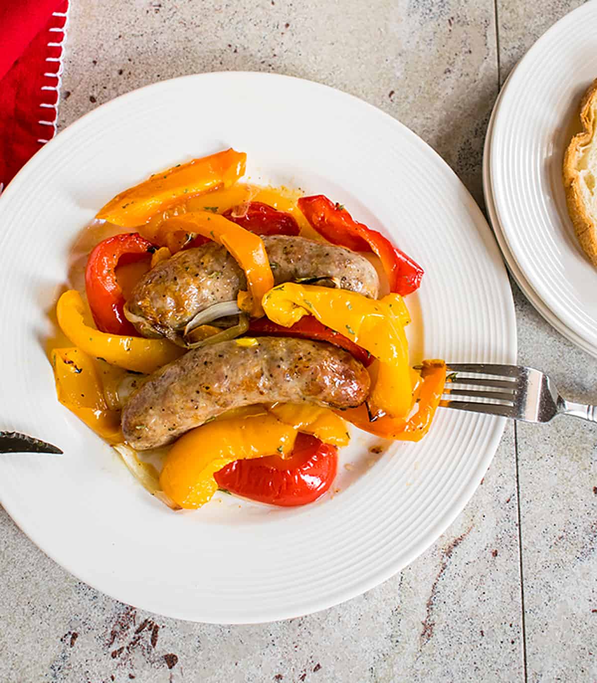 overhead view of sausages, peppers, onions on white plate with fork, knife