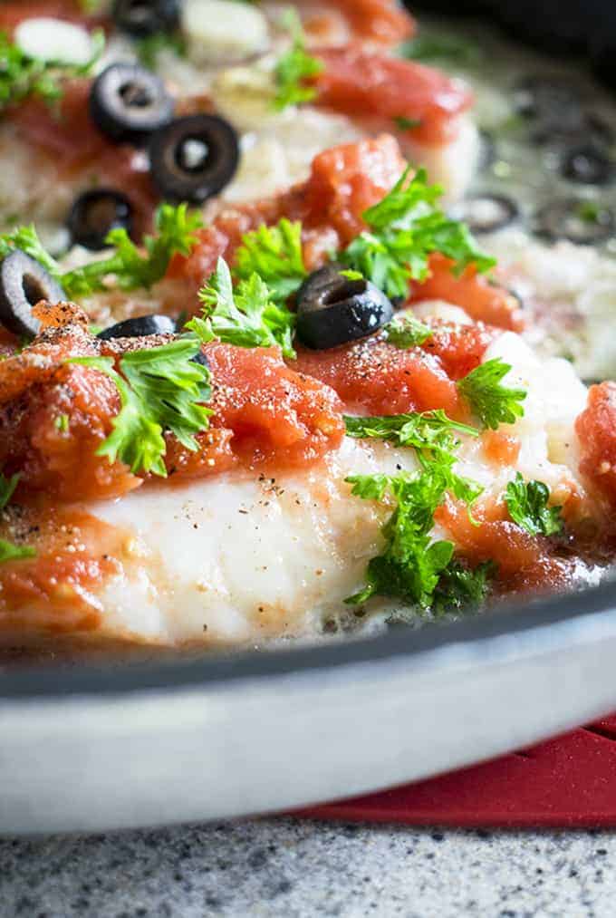 skillet of sauteed cod topped with tomatoes, parsley and olives