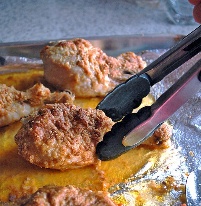 Tongs grabbing a Parmesan Chicken Drumstick with Garlic Butter from sheet pan