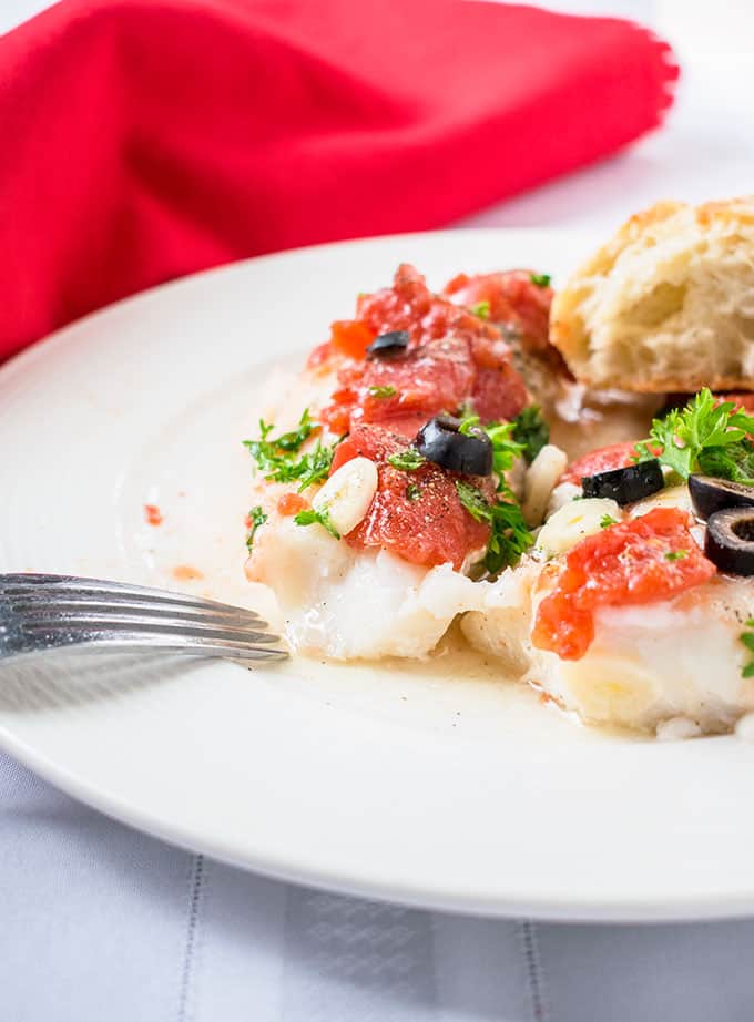 Sauteed Cod with tomatoes, parsley and olives on a plate with fork