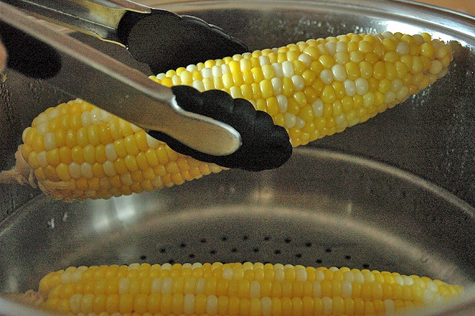 Tongs taking corn on the cob out of the pot
