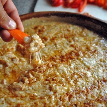 Hand dipping a carrot slice in Meatless Clams Casino Dip