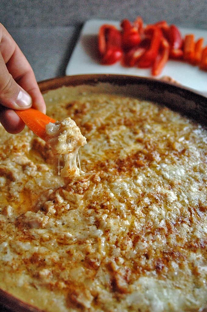 Hand dipping a carrot slice in Meatless Clams Casino Dip