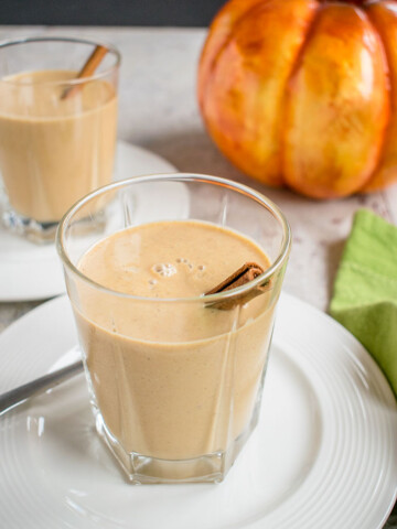 two glasses of pumpkin smoothies with cinnamon sticks on plates