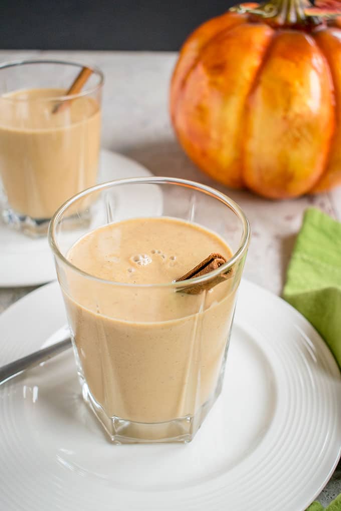 two glasses of pumpkin smoothies with cinnamon sticks on plates