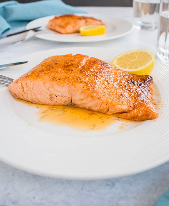two plates of 10-minute maple-glazed salmon with slices of lemon
