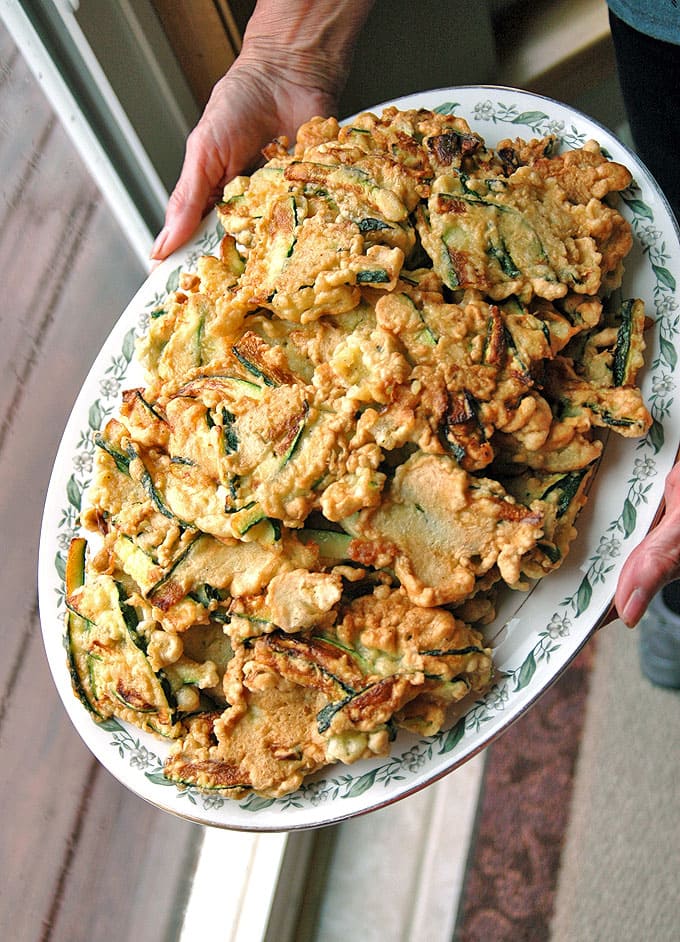 Hands holding a platter of zucchini fritters