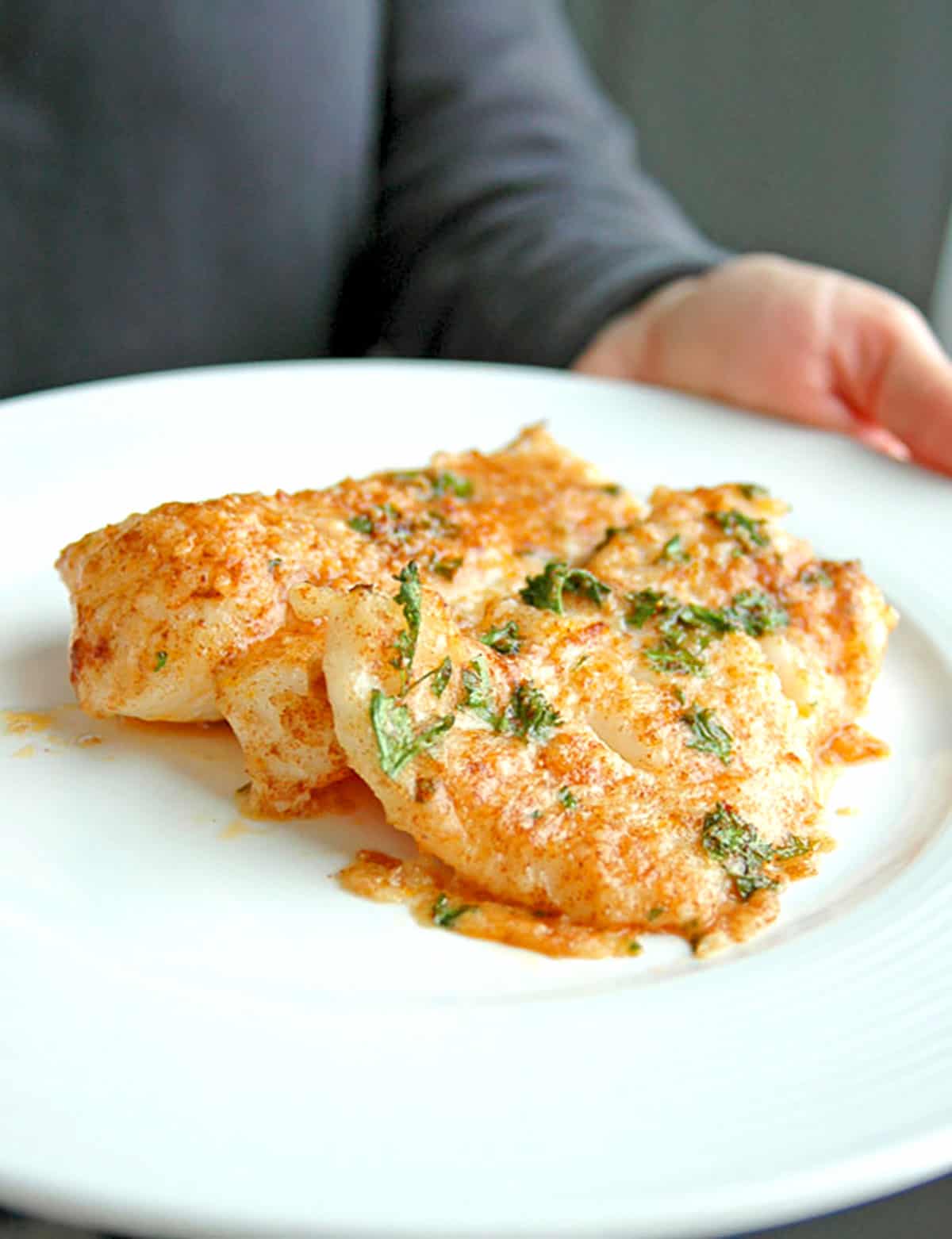 Plate of baked Lemon Parmesan Cod being held 