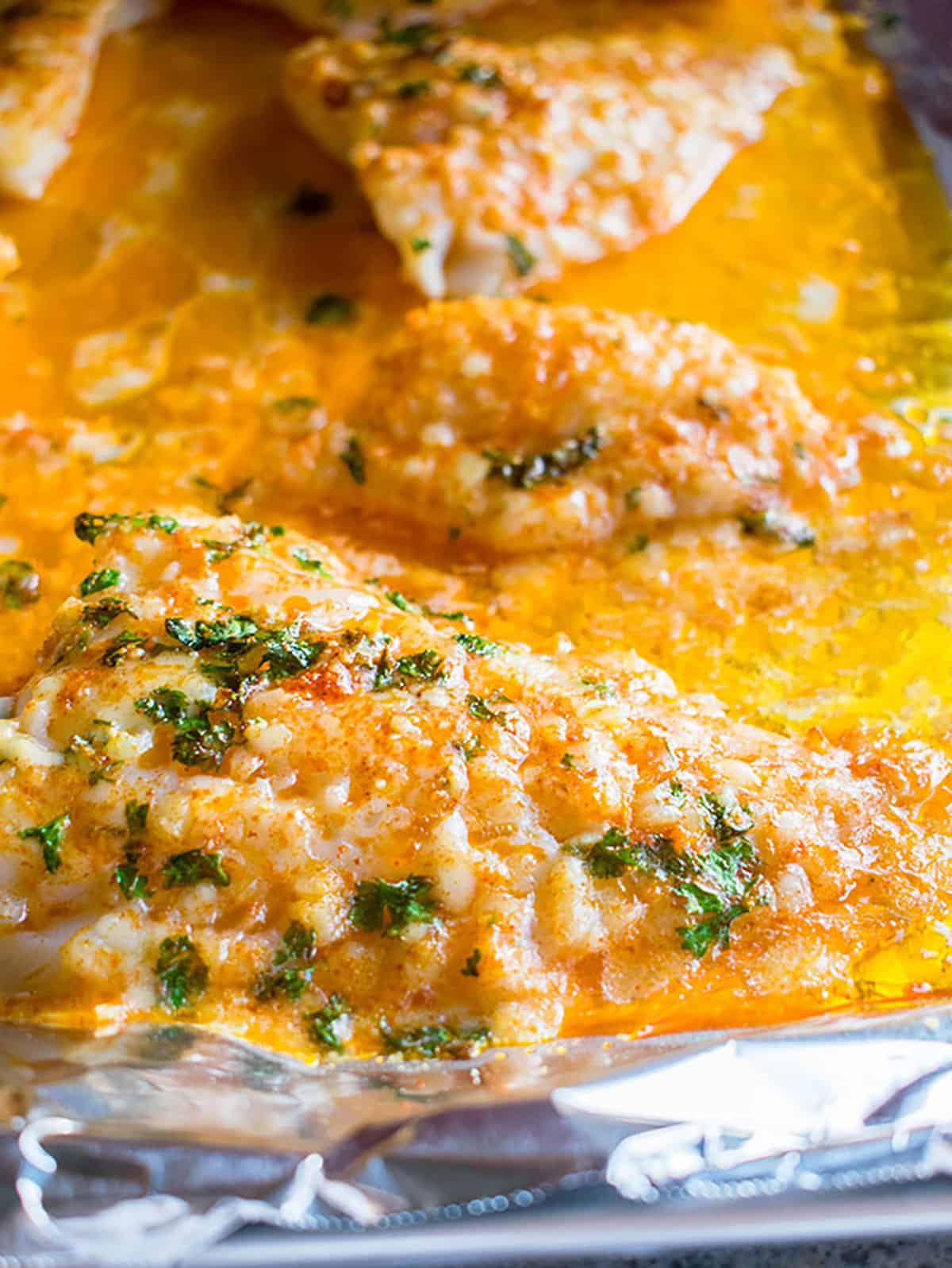 A close-up photo of baked Lemon Parmesan Cod sitting in a sheet pan of melted butter