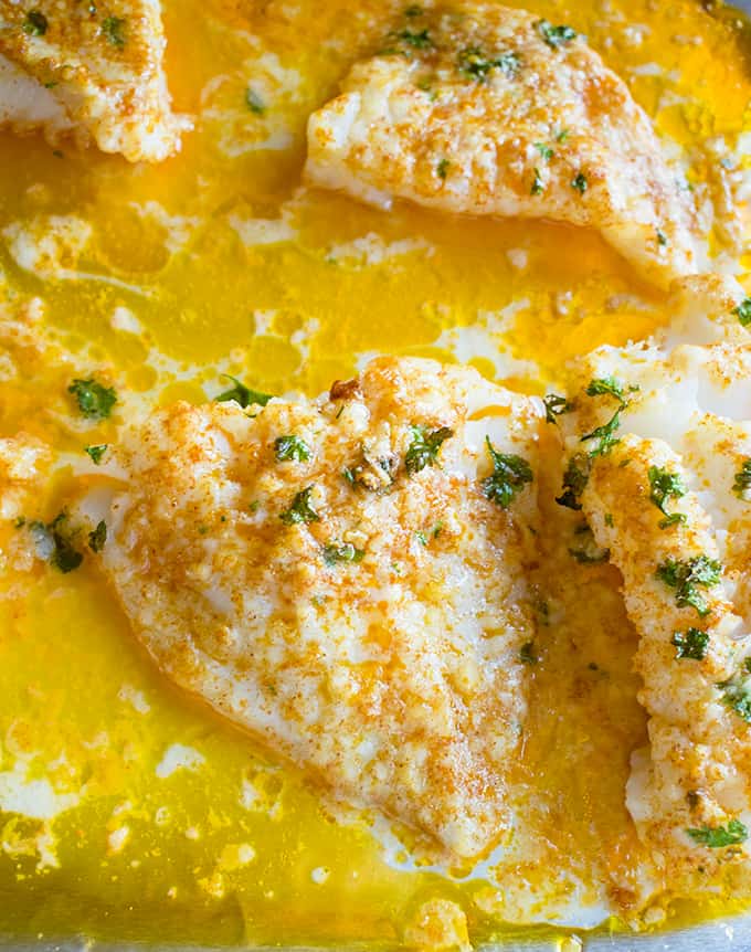 close-up of baked lemon parmesan cod with melted garlic butter in a sheet pan