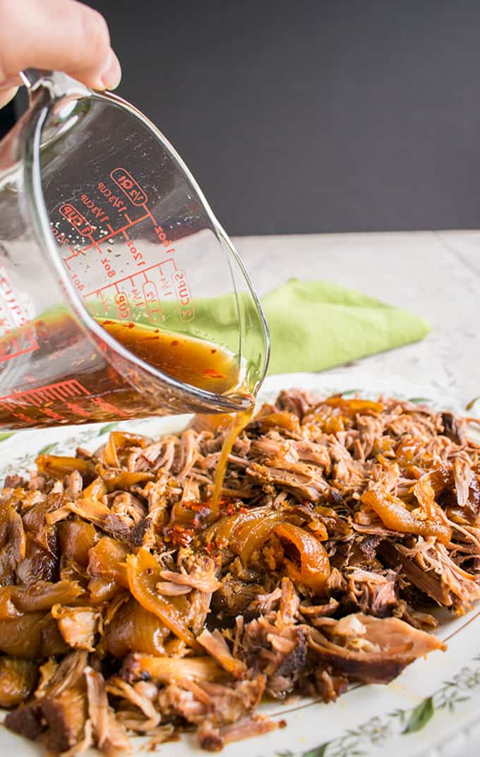 Cooked Carolina pulled pork on a platter being dressed with vinegar mixture