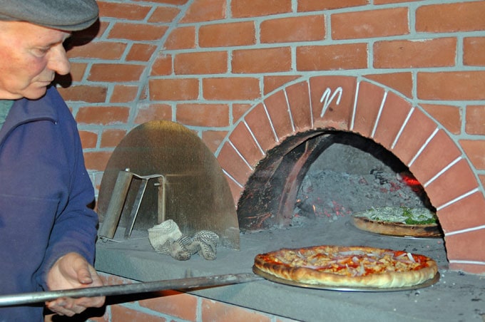 man putting pizza into brick oven