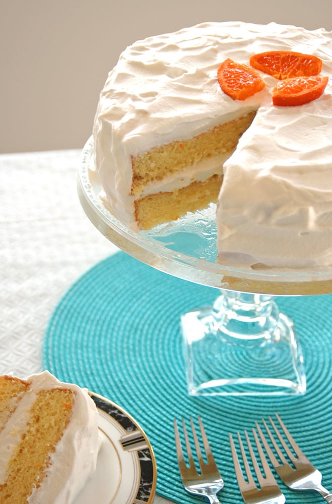 Orange Torte with Whipped Cream with piece taken out on a cake stand