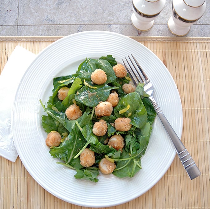 overhead view of breaded scallops over salad with lemon vinaigrette on a plate with fork