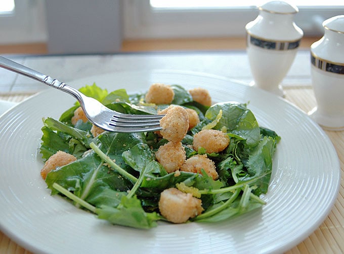 fork picking up a breaded scallop over salad with lemon vinaigrette 