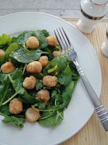 breaded scallops over salad with lemon vinaigrette on a plate with fork