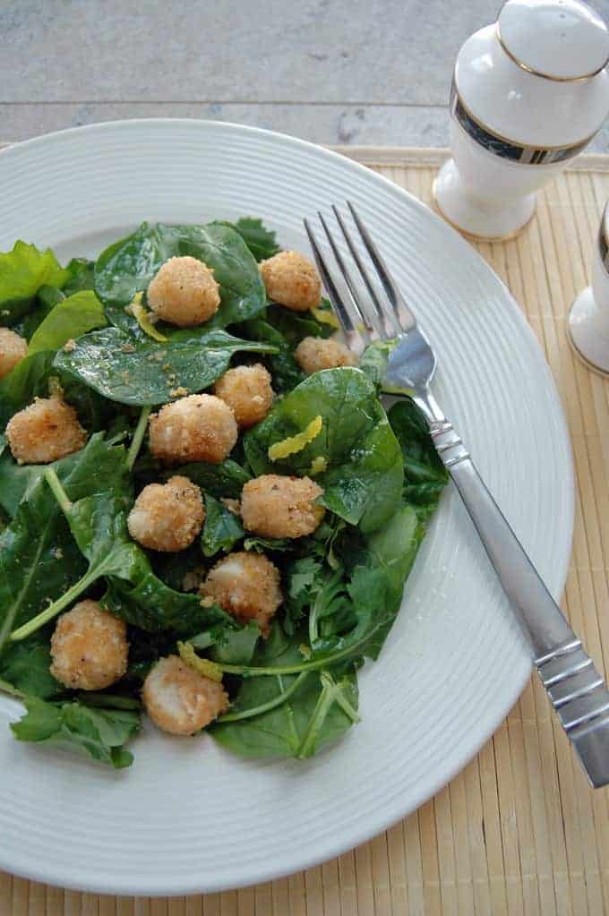breaded scallops over salad with lemon vinaigrette on a plate with fork.