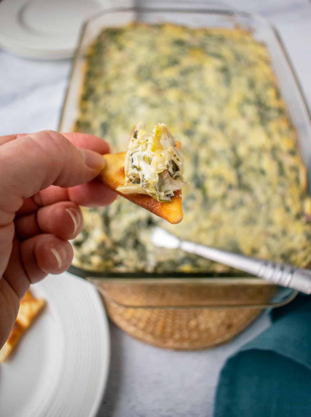 Photo of hand holding pita cracker with Asiago Spinach and Artichoke Dip