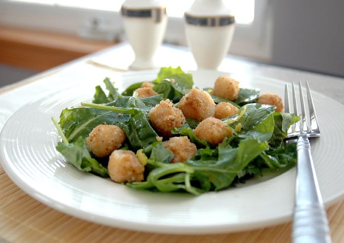 side view of breaded scallops over salad with lemon vinaigrette on a plate