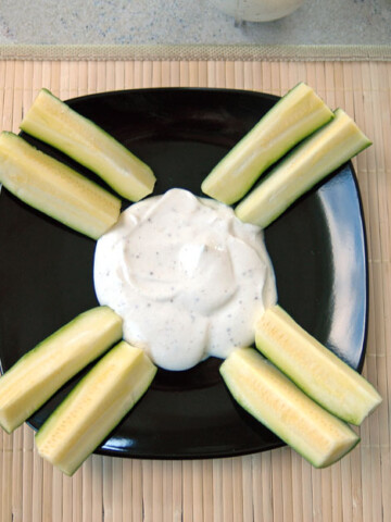 ranch dressing on a black plate with sliced zucchini