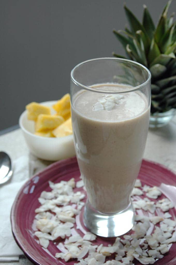 close-up of a glass of Pina Colada and Banana Breakfast Smoothie on a plate with coconut shavings and pineapple