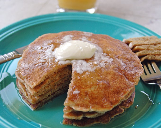 stack of Cinnamon Almond Multigrain Pancakes covered in butter and syrup with knife and fork