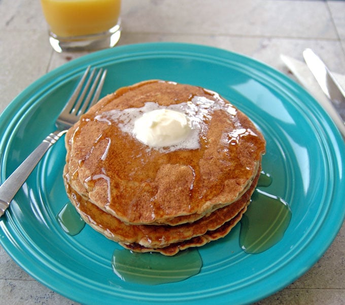 stack of Cinnamon Almond Multigrain Pancakes covered in butter and syrup on a plate with a fork