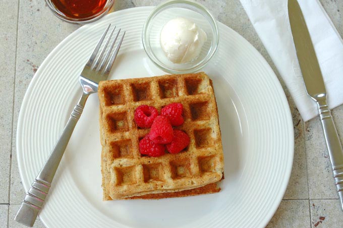 overhead view of Buttermilk Whole Grain Waffles topped with raspberries on a plate with butter and fork 