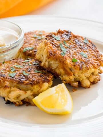 three crab cakes on plate with lemon, mayo
