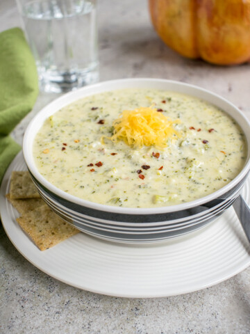 bowl of broccoli-cheddar soup on a plate with crackers