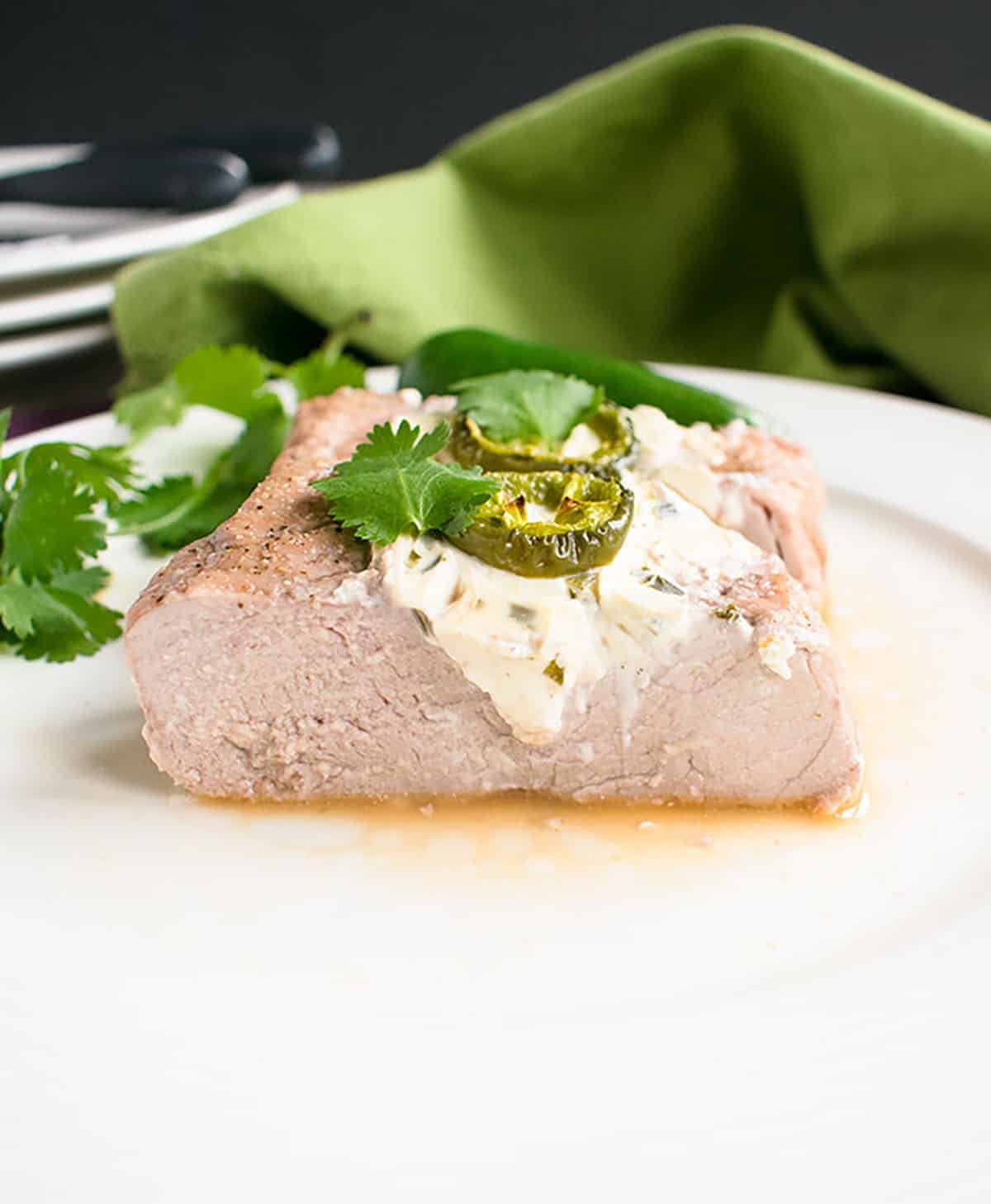 sliced pork tenderloin with cream cheese and jalapenos on a plate in front of a napkin