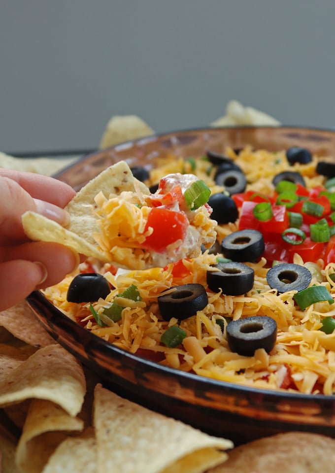 chipful of 7-Layer Taco Dip being taken from the dish