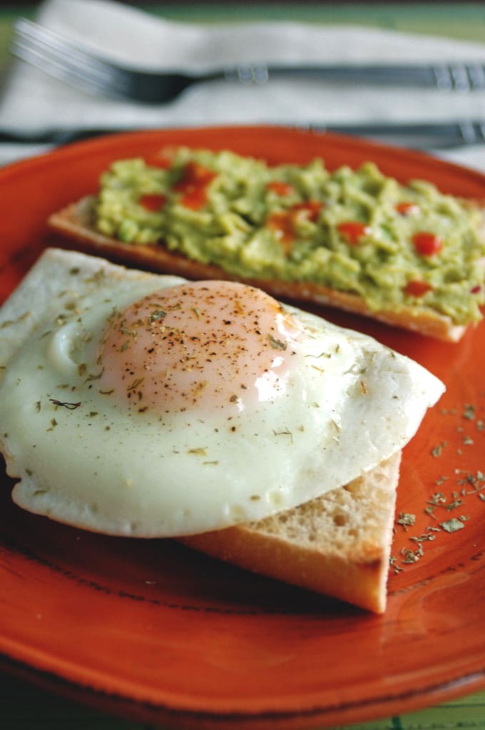 Basted egg on toast in front of guacamole on toast on a red plate