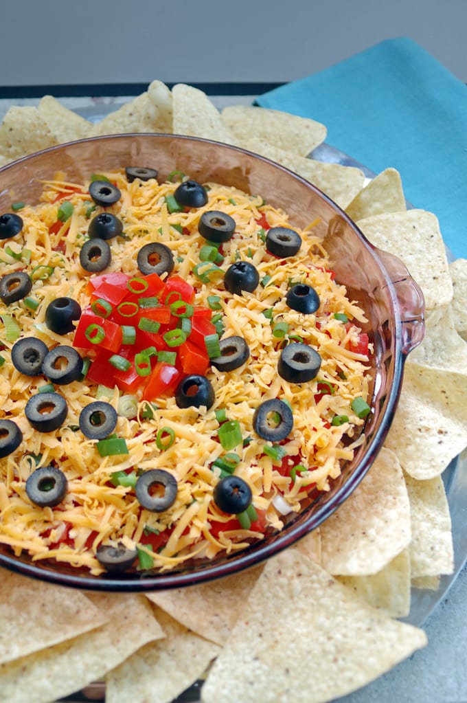 Tortilla chips surrounding a glass container of 7-Layer Taco Dip