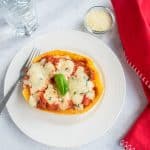 Spaghetti squash lasagna boat on a plate with a fork beside a glass of water, parmesan and apron