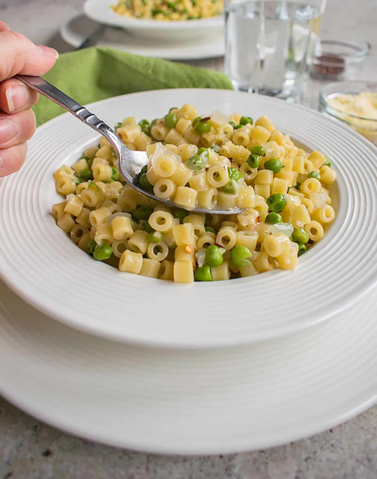 Hand taking a spoonful of pasta e piselli (pasta with peas) from a bowl on a plate