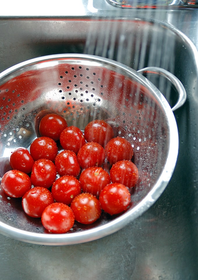 small tomatoes being rinsed in a strainer 