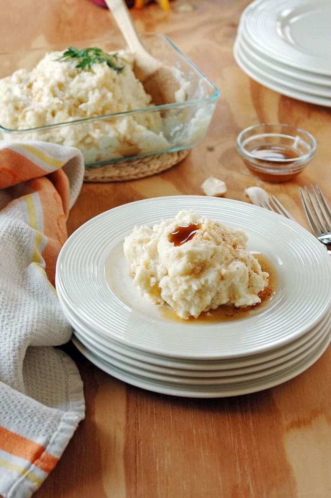 Amish Brown Butter Mashed Potatoes on a stack of plates in front of glass container of it 