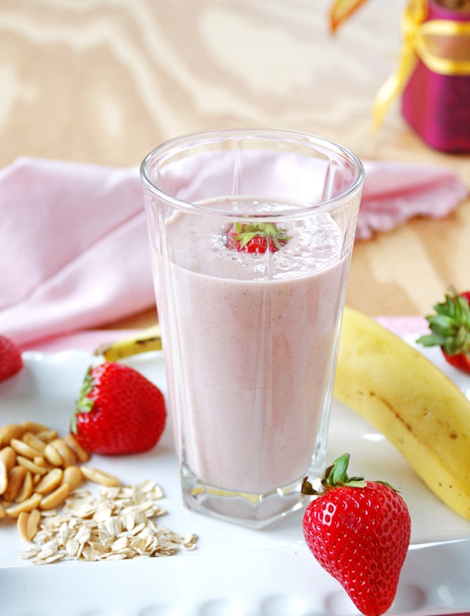 glass of Peanut Butter and Jelly Smoothie on a plate with banana, strawberries, peanuts and oats