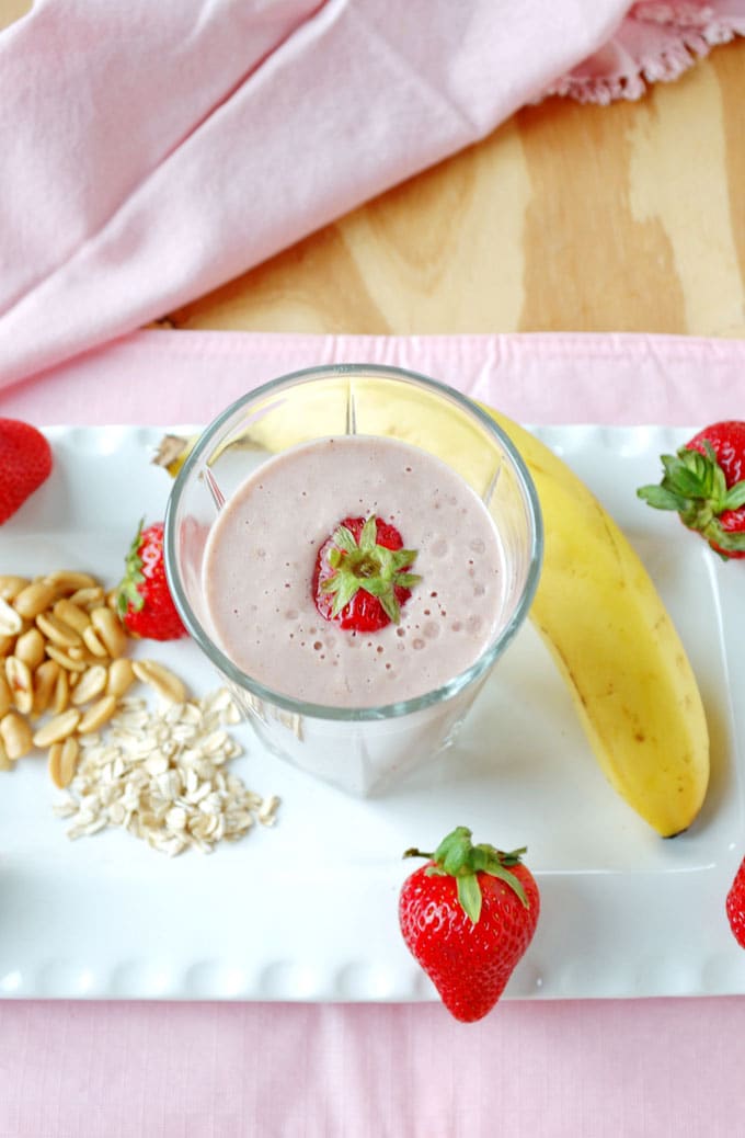 overhead view of glass of Peanut Butter and Jelly Smoothie, banana, strawberries, peanuts and oats