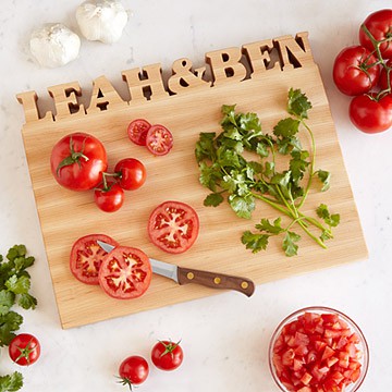 Custom cutting board saying \"Leah & Ben\" with a knife, tomatoes and parsley