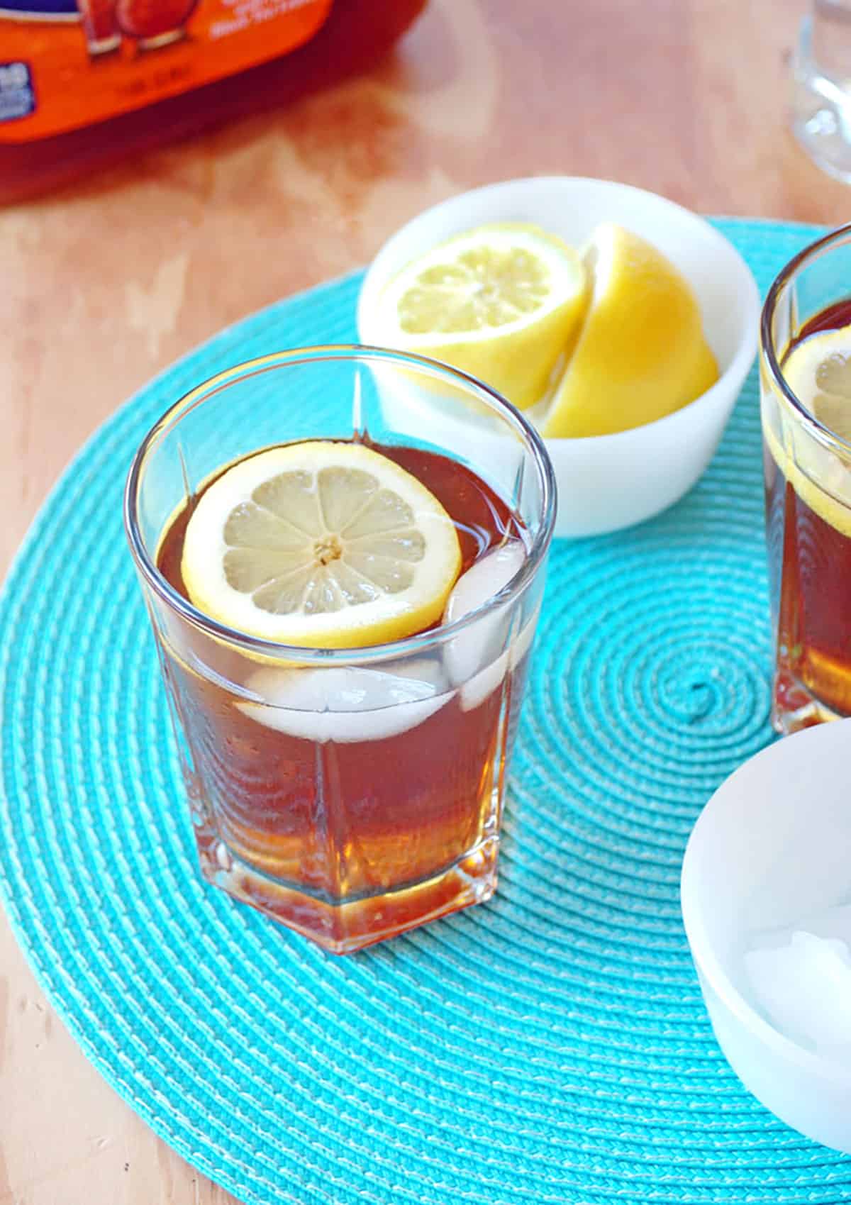 iced tea and rum cocktail with lemon wedge, container with two lemon halves