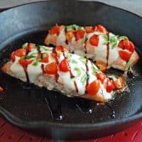 close-up of cast-iron skillet with two pieces of Salmon Caprese with Balsamic Glaze