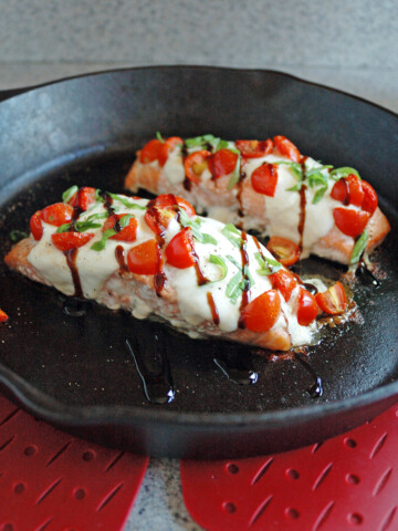 close-up of cast-iron skillet with two pieces of Salmon Caprese with Balsamic Glaze