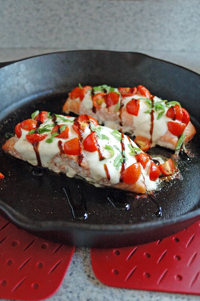 close-up of cast-iron skillet with two pieces of Salmon Caprese with Balsamic Glaze