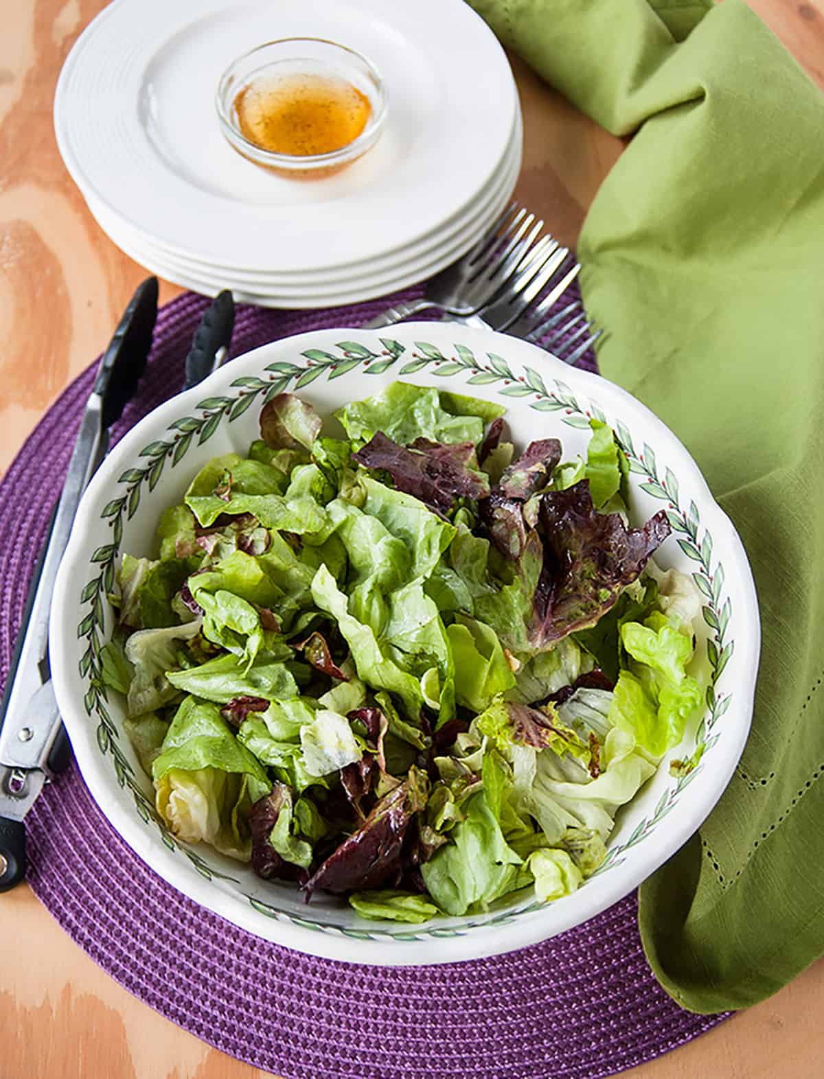 Italian Green Salad with Homemade Dressing in a bowl, tongs, stack of plates with dressing on top