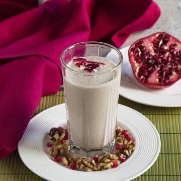 Pomegranate Smoothie with Banana and Walnuts in a glass surrounded by pomegranate and walnuts